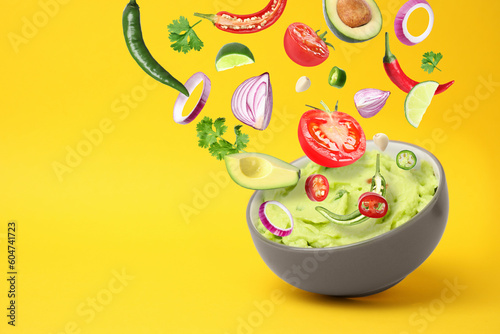 Delicious guacamole with flying ingredients on yellow background  space for text