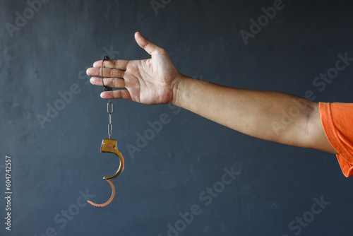 Fotografia Hand of prisoner man wearing orange clothes holding opened handcuffs