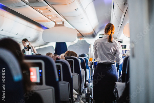 Interior of airplane with passengers on seats and stewardess in uniform walking the aisle, serving people. Commercial economy flight service concept photo