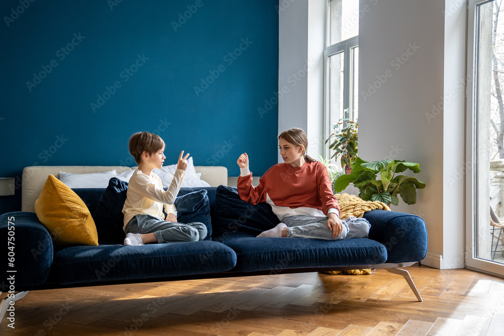 Children siblings sitting on sofa playing fun kids game Rock Paper Scissors to determine who has to clean room, brother and sister spending time together at home, family leisure concept