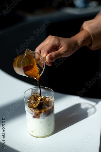 Pouring coffee into a glass of milk with ice cubes and honey
