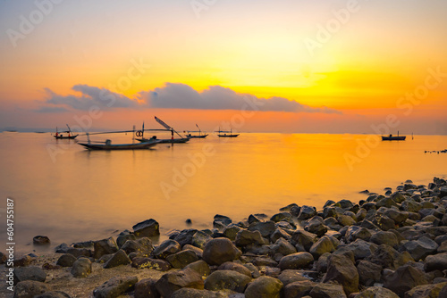 Beautiful cloudy sunrise with foreground of rocks and motion boats on the water in Kenjeran, Surabaya, Indonesia.