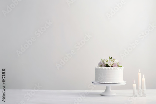 A white wedding cake stands on a white table in front of a white wall. Wedding background with lots of negative space.