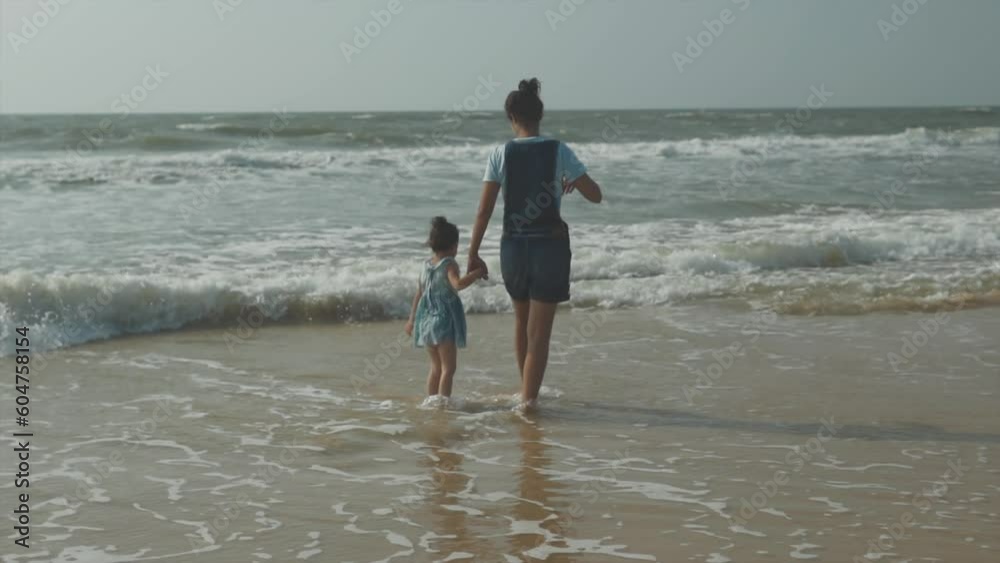 A slow-motion shot of a beautiful adult and young kid girl enjoying sea waves on the shore. A slow-motion shot of a beautiful adult and young kid girl enjoying sea waves on the shore.