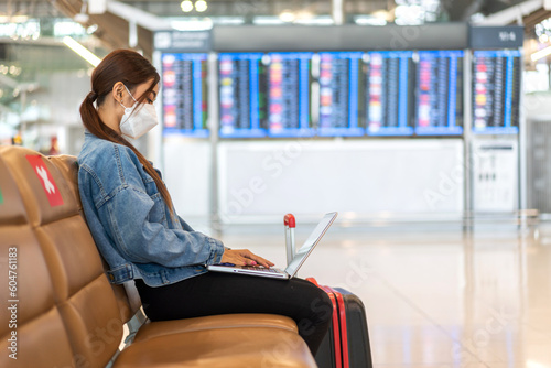 Young woman in quarantine for coronavirus wearing surgical mask face protection during virus pandemic with social distancing use laptop work with luggage wait flight travel at airport