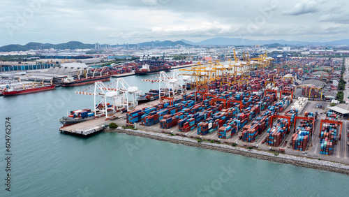 commercial port load and unloading cargo from container ship import and export by crane for distributing goods by trailers transported to customers and dealers, aerial view from drone.