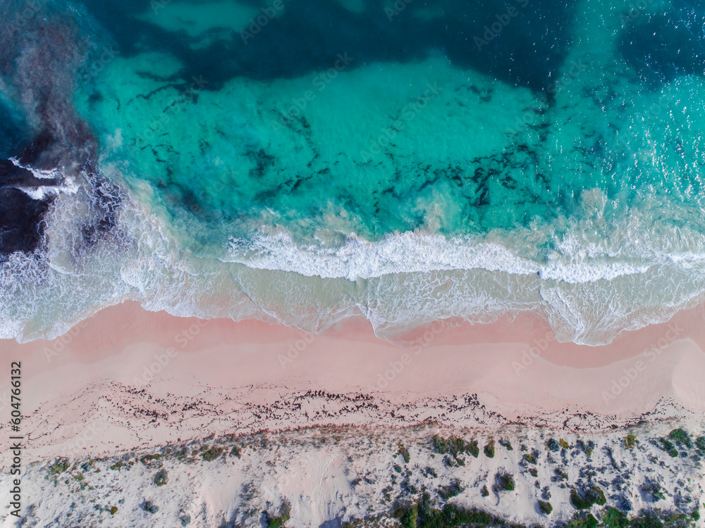 Aerial view of pink sandy beach with waves. Sunny day in summer with transparent tropical blue water. Summer seascape beautiful waves, blue sea water on a sunny day. Top view from drone. Sea aerial