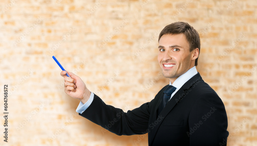 Image of business man in black confident suit, necktie, show pointing advertising product, on brown bricks wall office background. Copy space, slogan text area. Image of business man in black confident suit, necktie, show pointing advertising product, on brown bricks wall office background. Copy space, slogan text area.
