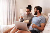 Laptop, watching movie and popcorn with laughing couple in bed for streaming, relax or internet. Subscription, happy or comic man and woman at home for social media, funny and free time on weekend