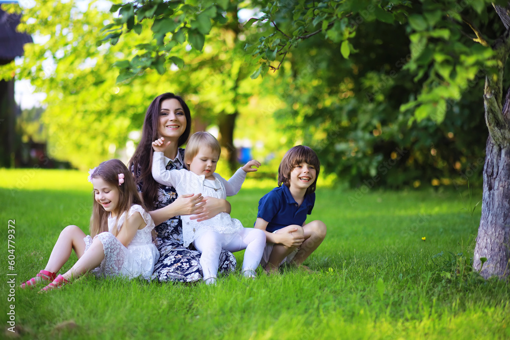 Young large family on a summer morning walk. Beautiful mother with children is playing in the park.