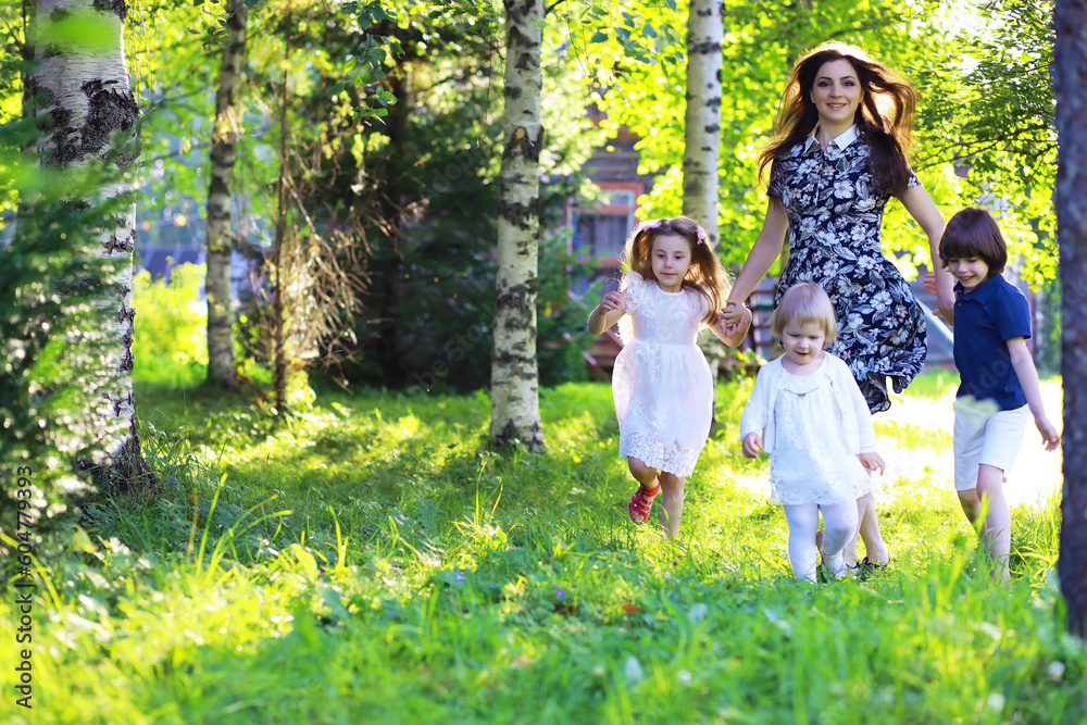 Fototapeta premium Young large family on a summer morning walk. Beautiful mother with children is playing in the park.