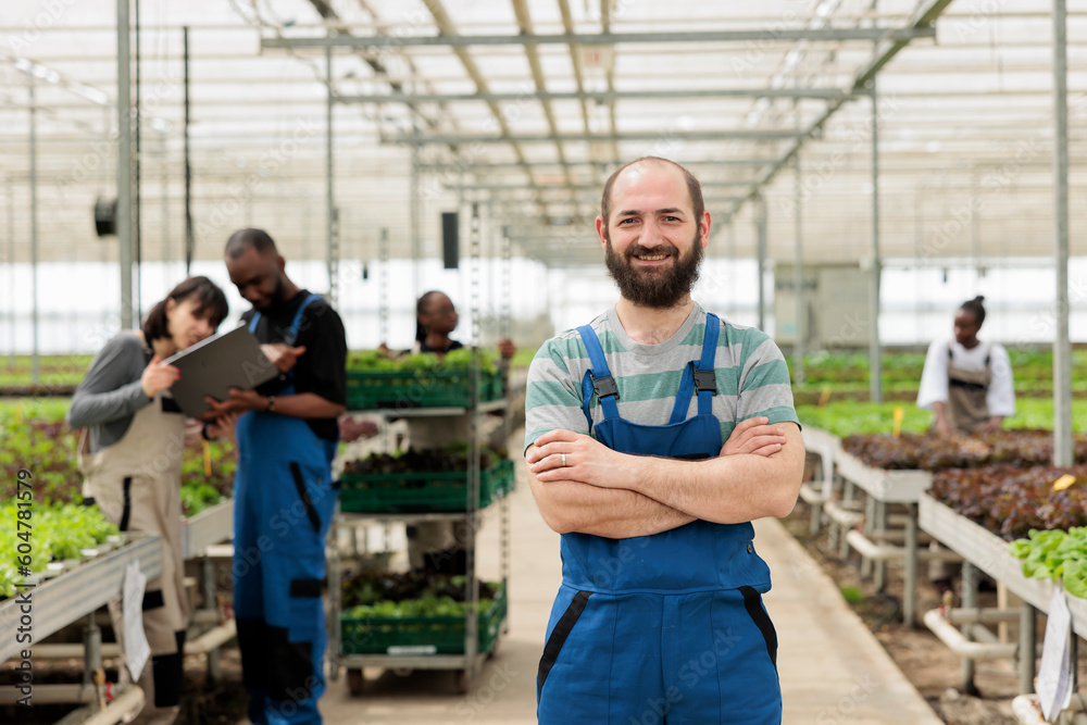 Smiling farm worker in green bio eco friendly agriculture organic hydroponic greenhouse with group of farmers. Locally grown chemical free vegetable crops using recycled water and non-GMO fertilizer