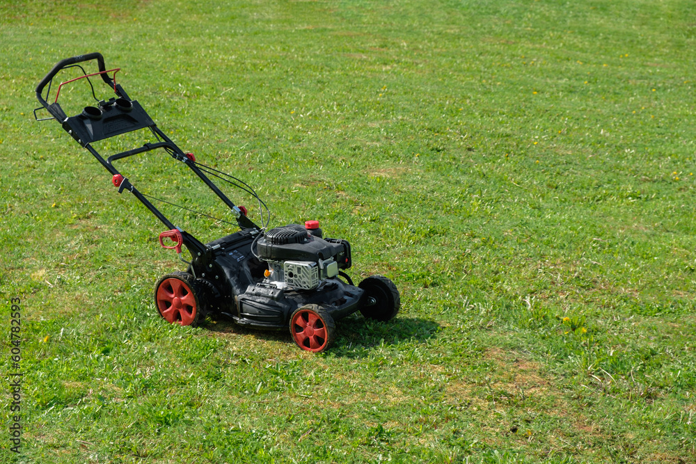Gasoline lawn mower on the freshly mowed backyard garden plot with copy space. Mowing dandelions. Lawn care, spring work in the garden. Gasoline lawn mower on the freshly mowed backyard garden plot with copy space. Mowing dandelions. Lawn care, spring work in the garden.
