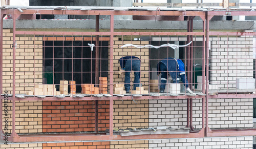 Workers lay brick walls at the construction site of a multi-storey building.