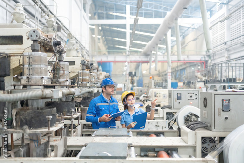 American engineers and Asian men and women consulting about work Pointing finger to destination, holding list note in plastic industry factory There is a working machine Wear uniforms and helmets.