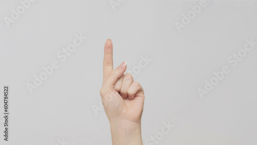 Hand gesture. One number. Woman counting pointing finger up on light gray background.