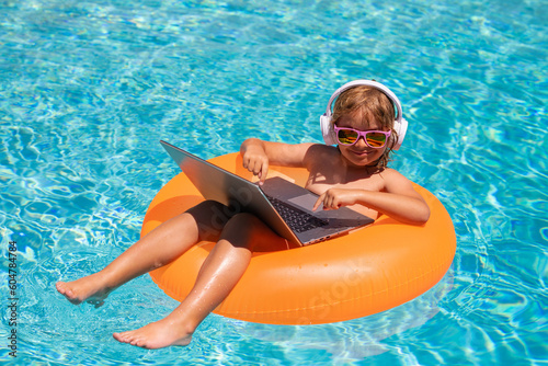 Work outside concept. Child working on laptop computer at poolside swimming pool. Summer online technology. Traveler relaxing on tropical sea beach in summer holidays vacation.