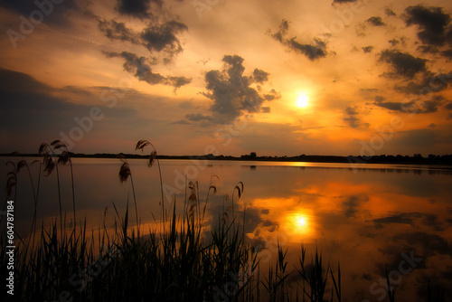 Fototapeta Naklejka Na Ścianę i Meble -  See im Abendrot - Sunset - Landscape - Beautiful Sunset scene over the lake and silhouette hills in the background - Sunrise over sea  - Colorful - Reed - Clouds - Sky - Sundown - Sun 