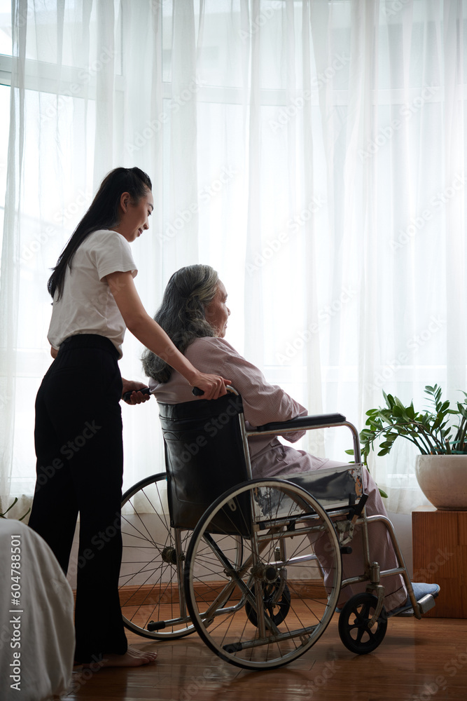 Daughter pushing wheelchair of her senior mother when visibly her in nursing home Daughter pushing wheelchair of her senior mother when visibly her in nursing home