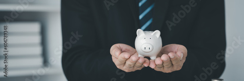 Young businessman's hand holding a piggy bank on the desk represents saving money financial concept business finance investment financial planning.