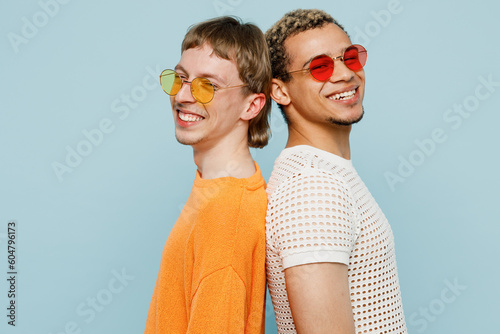 Side view young happy couple two gay men wearing casual clothes sunglasses together stand back to back isolated on plain blue color background studio portrait. Pride day june month love LGBTQ concept.
