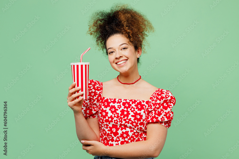 Young smiling happy fun woman she wearing casual clothes red blouse hold in hand cup of soda pop fizzy water isolated on plain pastel light green color background studio portrait. Lifestyle concept. Young smiling happy fun woman she wearing casual clothes red blouse hold in hand cup of soda pop fizzy water isolated on plain pastel light green color background studio portrait. Lifestyle concept.