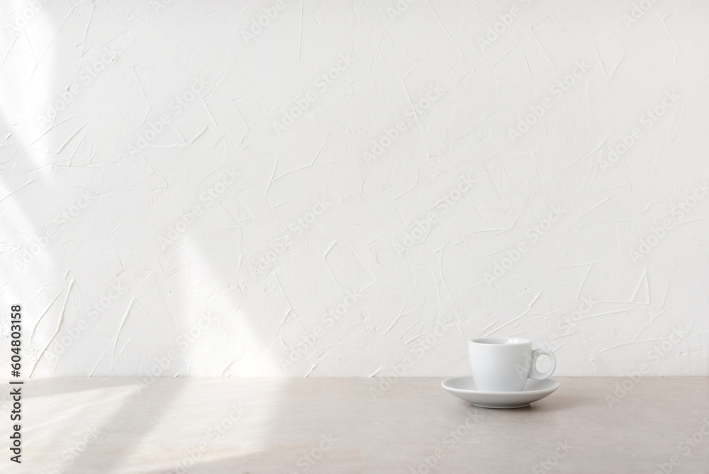 Minimalist nordic style good morning concept, cup with drink on beige table and empty white wall with aesthetic natural sunlight shadows and copy space - obrazy, fototapety, plakaty 