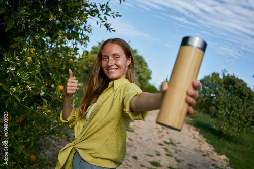 Smiling woman showing wooden thermos in garden photo