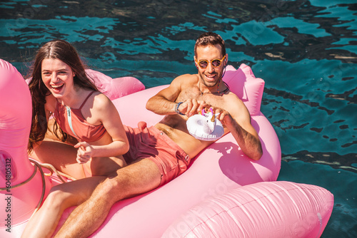 Couple floating on flamingo air mattress in sea at sunny day