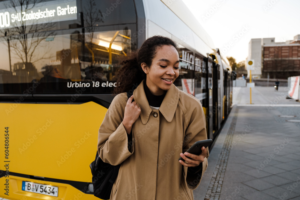 Obraz premium Smiling afro girl using smartphone while standing outdoors