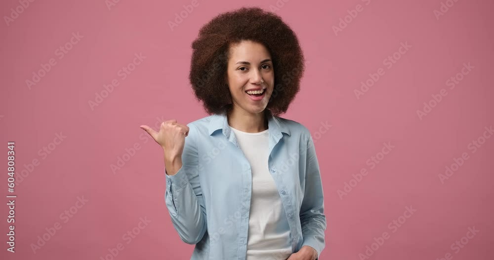 Cheerful expressive young african american woman in denim jacket white t-shirt pointing thumb aside on copy space workspace area isolated on pink studio background Cheerful expressive young african american woman in denim jacket white t-shirt pointing thumb aside on copy space workspace area isolated on pink studio background