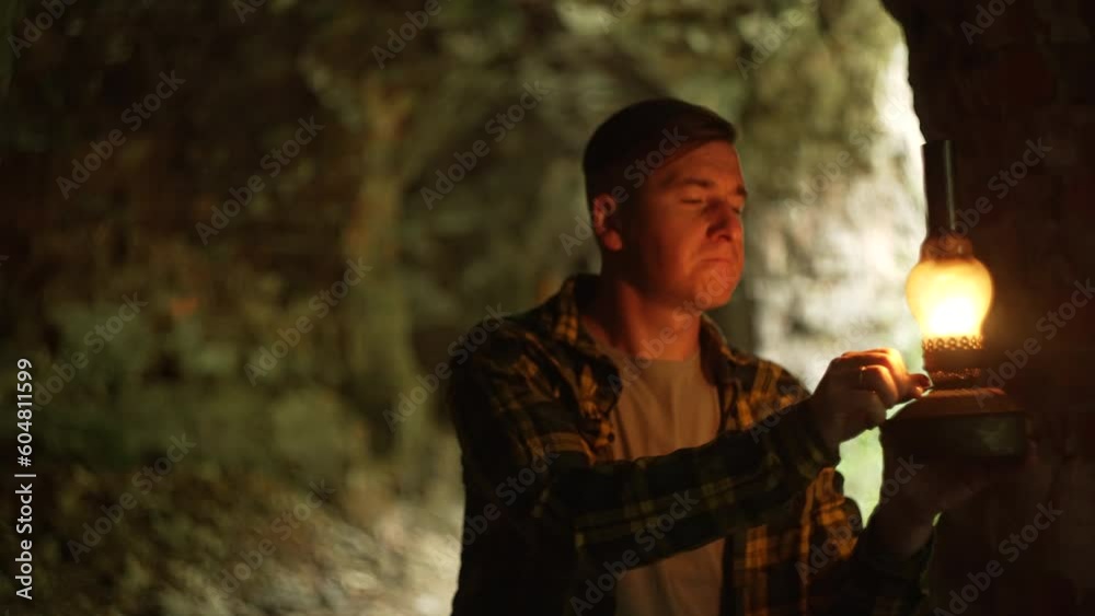 A man in a dungeon, holding a gas lamp. Exploring catacombs or old tunnels. The flickering light of a kerosene lamp. A mystical situation. Expedition on the abandoned territory. 4k 