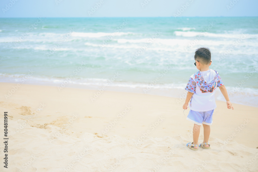 Asian boy wearing sunglasses is playing on a sandy beach near the sea. Asian boy wearing sunglasses is playing on a sandy beach near the sea.