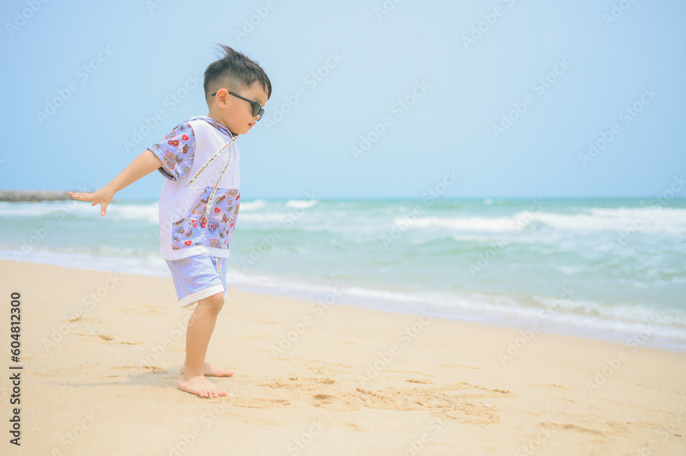 Asian boy wearing sunglasses is playing on a sandy beach near the sea. Asian boy wearing sunglasses is playing on a sandy beach near the sea.