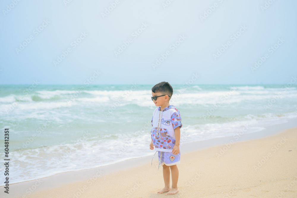 Asian boy wearing sunglasses is playing on a sandy beach near the sea. Asian boy wearing sunglasses is playing on a sandy beach near the sea.