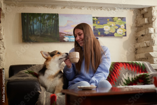 Cheerful young female sitting on a couch with a cute corgi dog. Loving owner having fun with the Pembroke Welsh Corgi puppy in a cafe © hurricanehank