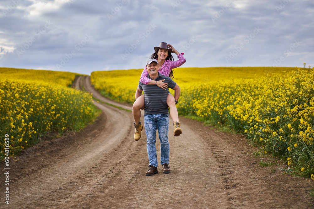 Fototapeta premium Farmers doing a piggyback ride through canola field