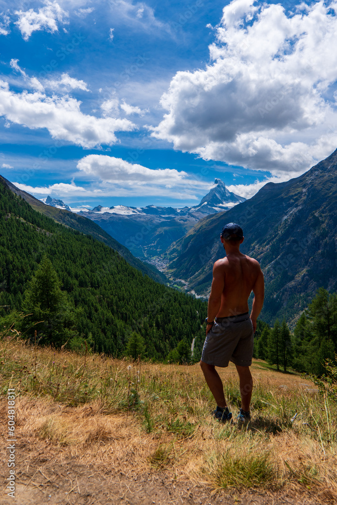 Travelling in Switzerland, a man with backpack standing on the rock looking at Matterhorn mountain view. Trekking in Zermatt, Switzerland