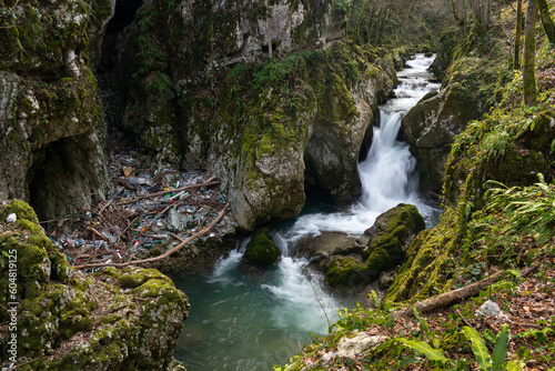 Waterfall with mossy rocks in mountain canyon and plastic waste problem  Svrakava river near Banja Luka