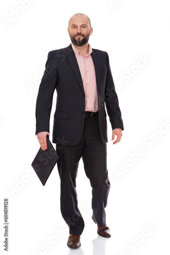 Full-length portrait of forty year old man in a business suit walking to the camera with laptop in his hand, isolated on white background. Bearde caucasian businessman posing in studio.