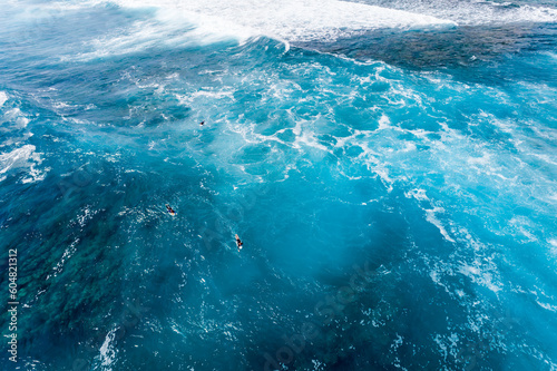 Big sea waves and dark blue water. Surfers paddling out in big surf.