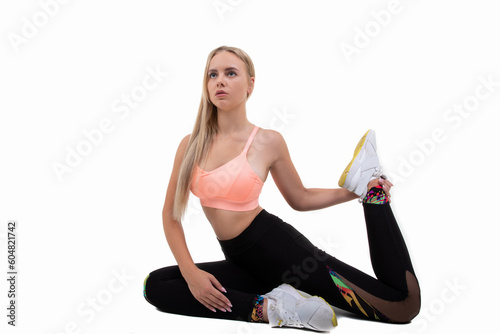 Sporty woman in a pink top, dark leggings and sneakers does stretches on a white background
