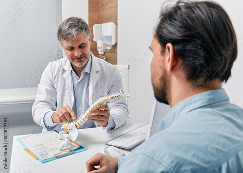 Obraz na płótnie Chiropractor explaining backbone problems using anatomical model of spine to patient while visit to osteopathy clinic