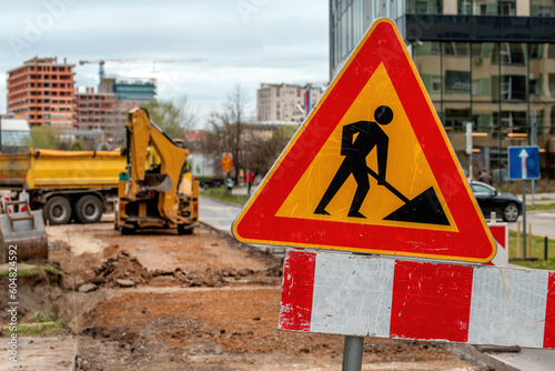 Men at work sign at roadworks and road maintenance construction site with trucks and machinery in background
