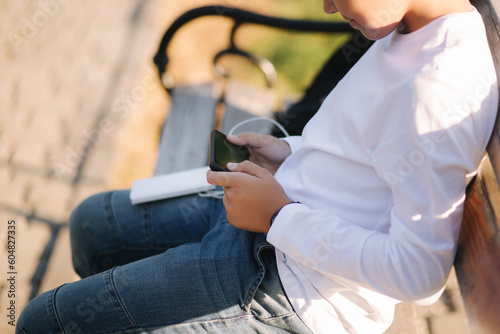 Teenage boy in white shirt use powerbank for charging his smartphone otside. Low battery on smartphone