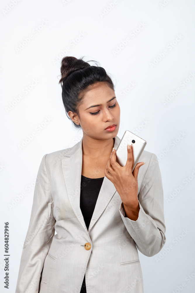 Corporate office lady with black hair having playful moment with pen, smart phone in formal wear wearing white blazer against white background.
