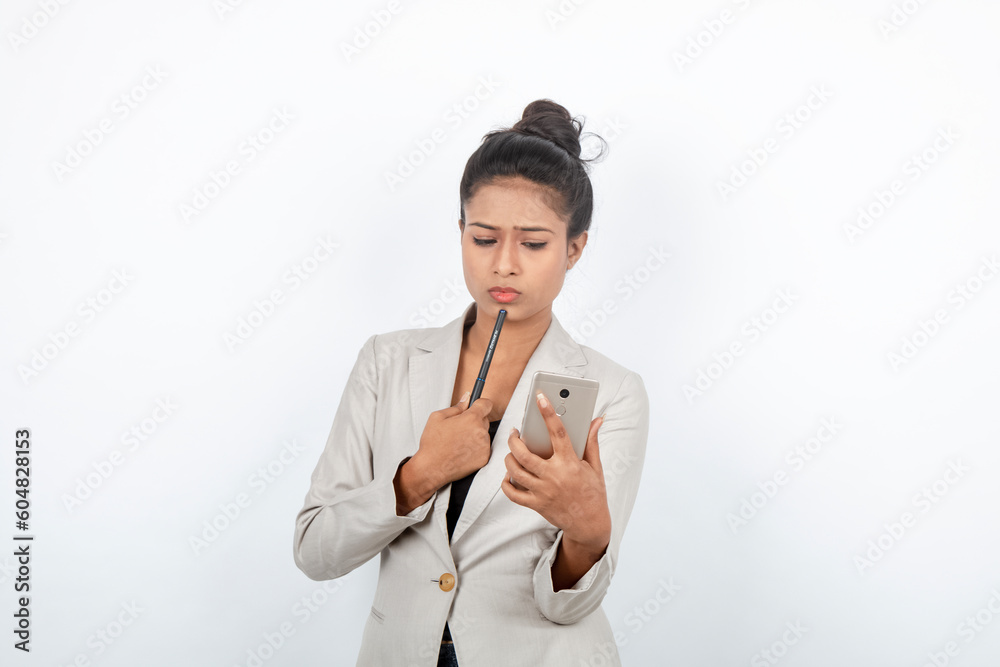 Corporate office lady with black hair having playful moment with pen, smart phone in formal wear wearing white blazer against white background. Corporate office lady with black hair having playful moment with pen, smart phone in formal wear wearing white blazer against white background.