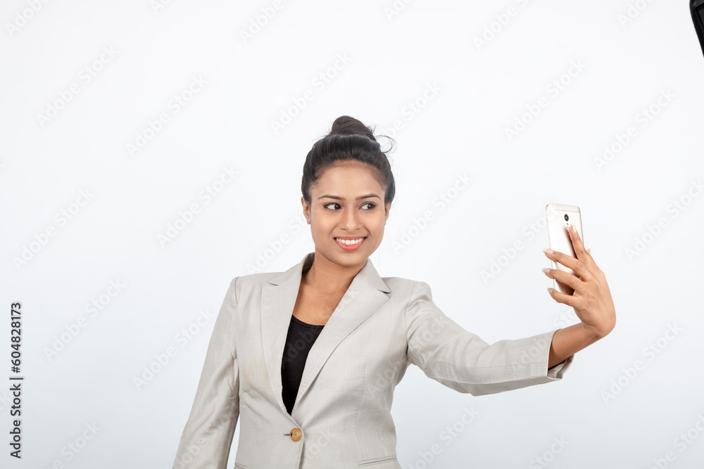 Corporate office lady with black hair having playful moment with pen, smart phone in formal wear wearing white blazer against white background. Corporate office lady with black hair having playful moment with pen, smart phone in formal wear wearing white blazer against white background.