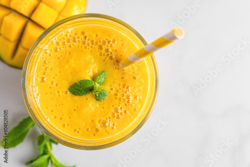 Fresh yellow summer mango smoothie in a glass with a straw and mint on white marble table. Top view