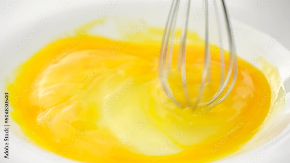 Chef mixing eggs with whisk in white plate, close up Chef mixing eggs with whisk in white plate, close up